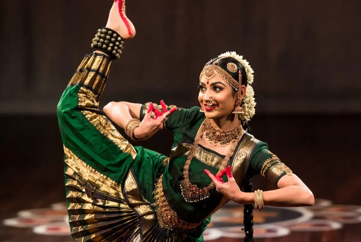 A Kuchipudi dancer performing the iconic Tarangam — balancing a water pot on the head and holding oil lamps while dancing on the rim of a brass plate, demonstrating the extraordinary skill and devotion at the heart of this classical Andhra tradition.